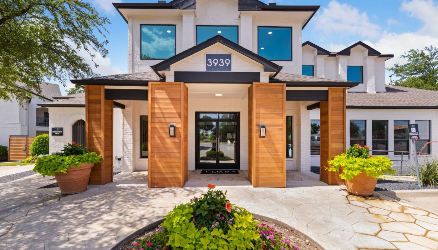 entrance to a building with large windows and lush landscaping surrounds